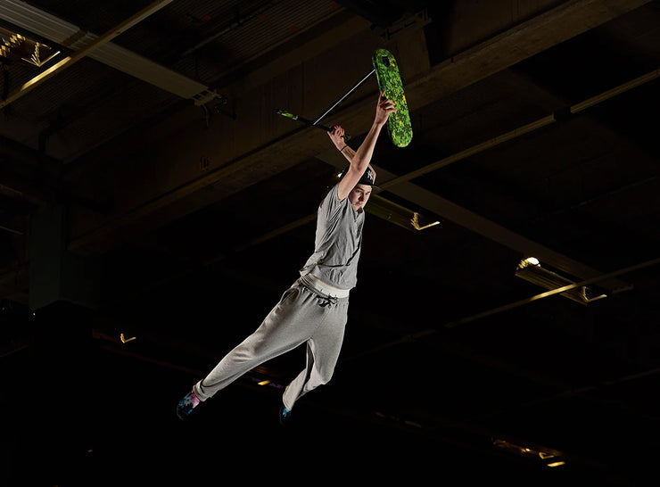 A rider performs a trick on the INDO PRO V2 Green Mamba trampoline trick scooter, capturing an exciting moment mid-air.